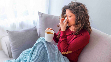 Woman not feeling well and blowing her nose, sitting on the sofa
